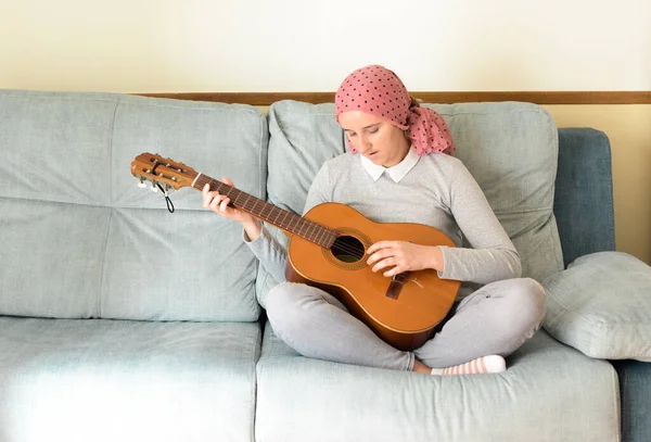 Portrait of a woman with cancer and depression locked in her home thinking. Pink headscarf. Playing the Spanish guitar. Fighting cancer.