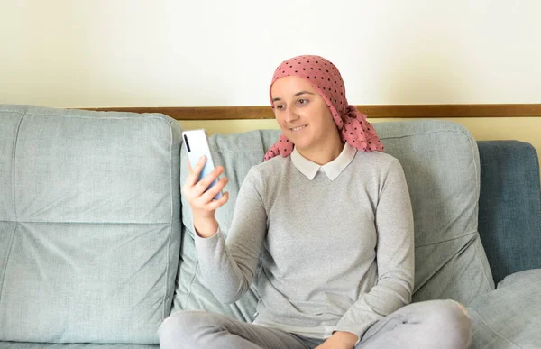 Portrait of a woman with cancer and depression locked in her home thinking. Pink headscarf. Looking at her cell phone. Fighting cancer.