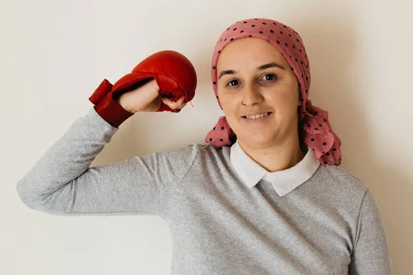 Portrait of a woman with cancer and depression locked in her home thinking. Pink head scarf and red boxing scarf. Showing muscle. Fighting cancer.
