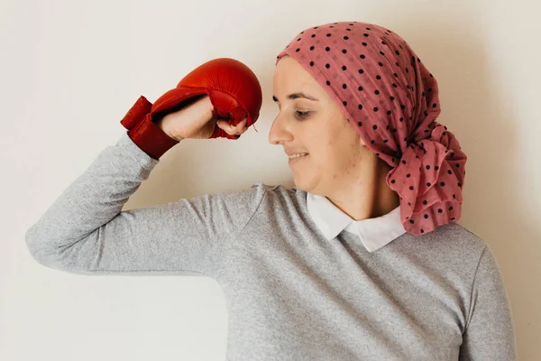 Portrait of a woman with cancer and depression locked in her home thinking. Pink head scarf and red boxing scarf. Showing muscle. Fighting cancer.