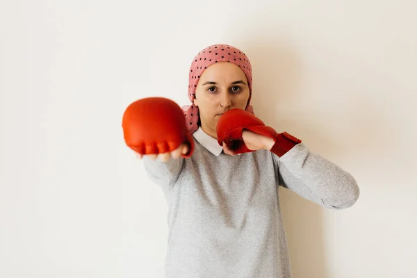 Portrait of a woman with cancer and depression locked in her home thinking. Pink headscarf and red boxing gloves. Fighting against cancer.