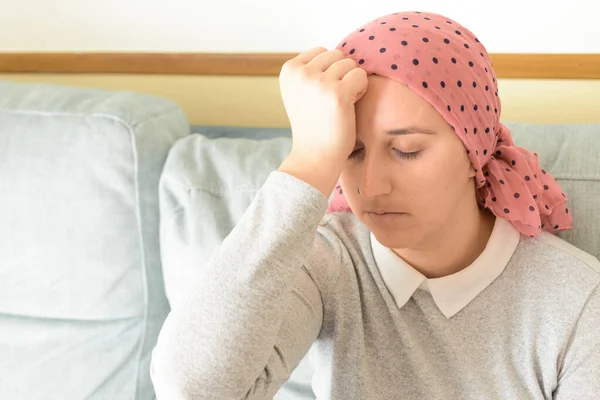 Portrait of a woman with cancer and depression locked in her home thinking. Worried and with a headache. Pink headscarf. Quarantine coronavirus.