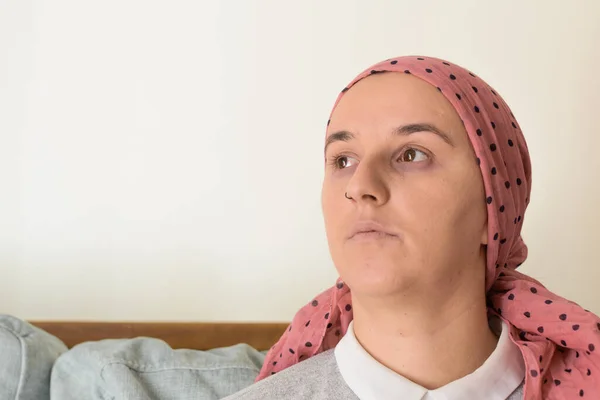 Portrait of a woman with cancer and depression locked in her home thinking. Pink headscarf. Quarantine coronavirus.