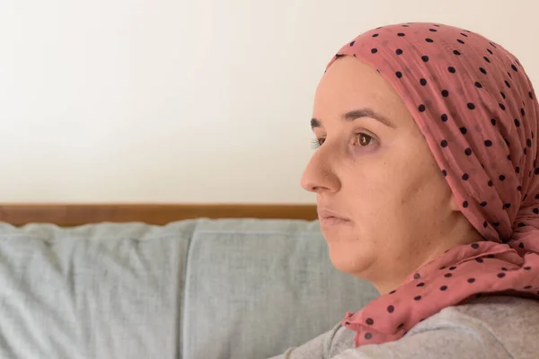 Portrait of a woman with cancer and depression locked in her home thinking. Pink headscarf. Quarantine coronavirus.
