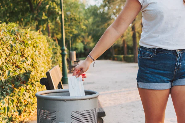 woman throwing a medical mask in the garbage can of a park.