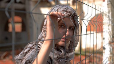 young refugee girl looking behind the fence clipart