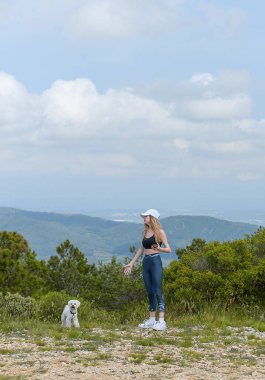Spor kıyafetli kız beyaz köpeğiyle eğleniyor.