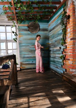 Çiçeklerin arka planında elinde kuş kafesi olan pembe Japon kimonolu bir kız.