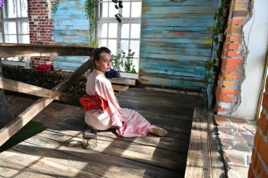 Çiçeklerin arka planında elinde kuş kafesi olan pembe Japon kimonolu bir kız.