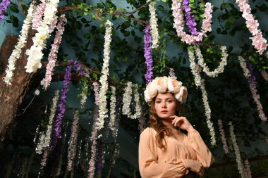 Bej elbiseli güzel bir kız ağaçların arasında bir çiçek çelengi içinde.