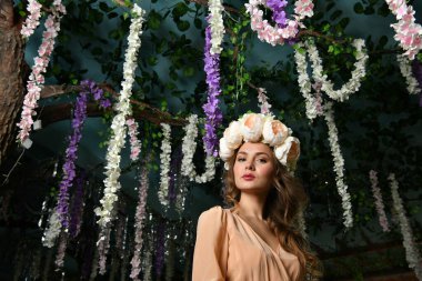 Bej elbiseli güzel bir kız ağaçların arasında bir çiçek çelengi içinde.