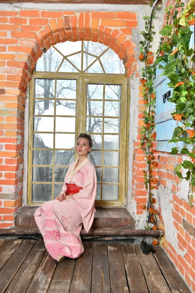 girl in pink japanese kimono on a background of flowers dreams at the window