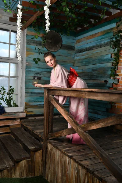 girl in pink japanese kimono on a background of flowers with a birdcage in her hands