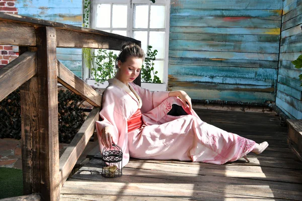 手に鳥かごを持った花を背景にピンクの日本の着物を着た女の子 — ストック写真