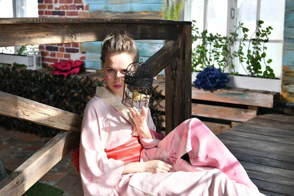 girl in pink japanese kimono on a background of flowers with a birdcage in her hands