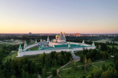 Şafak vakti insansız hava aracından çekilen yeşil tepedeki beyaz taş manastırın panoramik görüntüsü