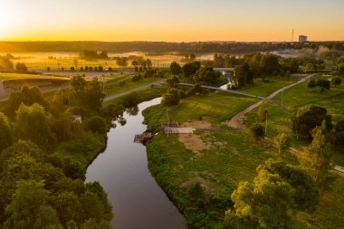 Şafakta insansız hava aracından alınan bir nehirle sisli yeşil alanların panoramik görüntüsü