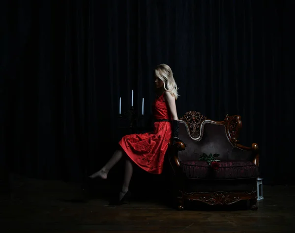 黒い背景にカンデラブラムの椅子に身を包んだ赤いドレスを着た美しい少女 — ストック写真