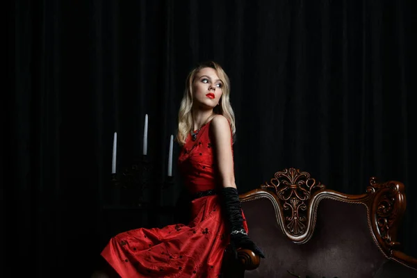 Piękna Dziewczyna Czerwonej Sukience Pozowanie Fotelu Kandelabrumem Czarnym Tle — Zdjęcie stockowe