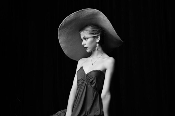 beautiful girl in a wide-brimmed hat and in a burgundy evening dress posing on a black background