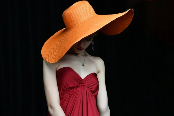 beautiful girl in a wide-brimmed hat and in a burgundy evening dress posing on a black background