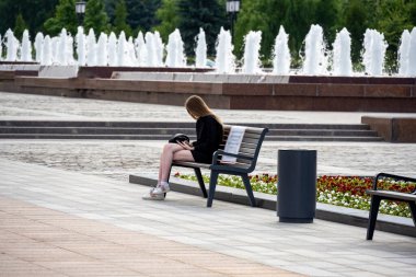 Siyah giyen kız bankta oturuyor.