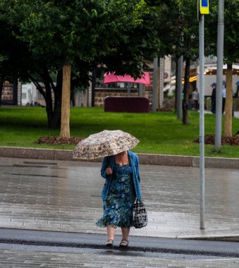 Siyah şemsiyeli yaşlı bir kadın karşıdan karşıya geçiyor.