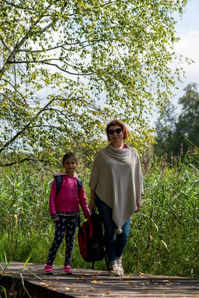 a girl and grandmother walk along the path between the swamps in the reserve on excursions