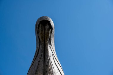 Kafası örtülü ve yüzü ellerle kaplı bir kadının metal heykeli.