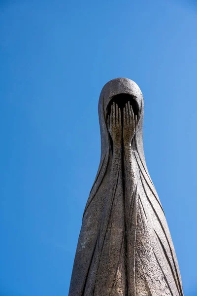 metal statue of a woman with her head covered and her face covered with hands