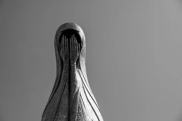 metal statue of a woman with her head covered and her face covered with hands