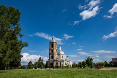 Mavi gökyüzüne karşı yeşil ağaçların arasında eski bir malikanenin kalıntıları.