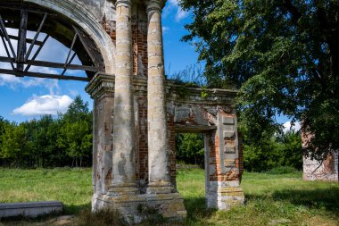 Mavi gökyüzüne karşı yeşil ağaçların arasında eski bir malikanenin kalıntıları.