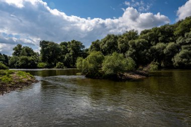 Mavi gökyüzüne karşı yeşil ağaçların arasında eski bir malikanenin kalıntıları.