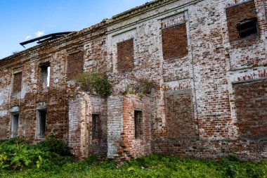 Mavi gökyüzüne karşı yeşil ağaçların arasında eski bir malikanenin kalıntıları.