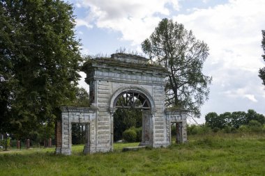 Mavi gökyüzüne karşı yeşil ağaçların arasında eski bir malikanenin kalıntıları.