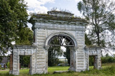 Mavi gökyüzüne karşı yeşil ağaçların arasında eski bir malikanenin kalıntıları.
