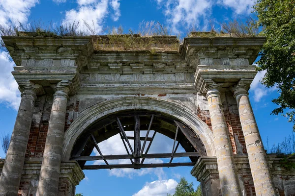 Mavi gökyüzüne karşı yeşil ağaçların arasında eski bir malikanenin kalıntıları.