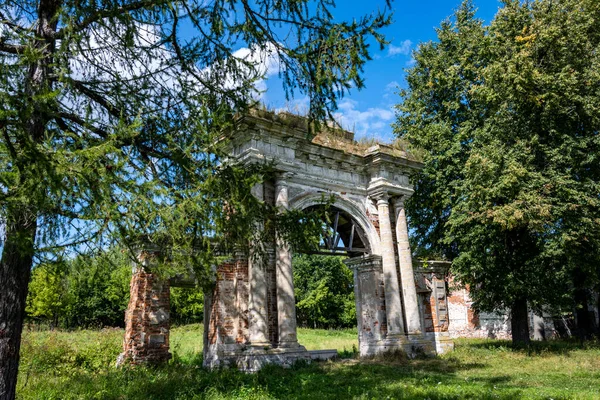 Mavi gökyüzüne karşı yeşil ağaçların arasında eski bir malikanenin kalıntıları.
