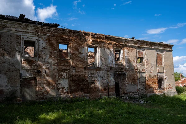 Mavi gökyüzüne karşı yeşil ağaçların arasında eski bir malikanenin kalıntıları.