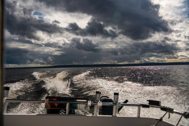 Mavi suların ve mavi gökyüzünün arka planında yüksek süratli bir teknenin yanından geçen gemilerin bulunduğu adalar.