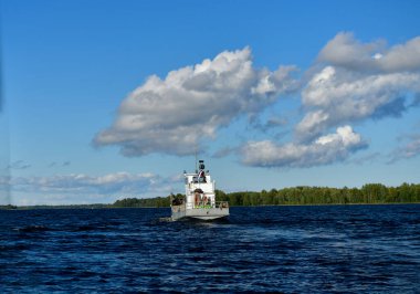 Mavi suların ve mavi gökyüzünün arka planında yüksek süratli bir teknenin yanından geçen gemilerin bulunduğu adalar.