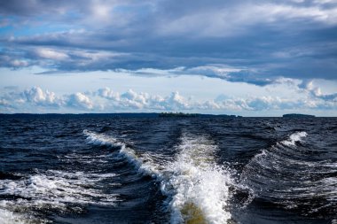 Mavi suların ve mavi gökyüzünün arka planında yüksek süratli bir teknenin yanından geçen gemilerin bulunduğu adalar.