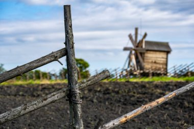Yeşil bir tepenin arkasındaki çitin arkasında mavi gökyüzü arka planına karşı klasik ahşap değirmen.