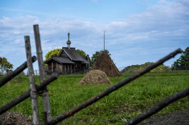 Yeşil bir tepenin arkasındaki çitin arkasında mavi gökyüzü arka planına karşı klasik ahşap değirmen.