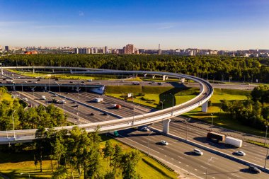 Arkaplanda insansız hava aracından çekilen şehirle karmaşık bir karşılıklı geçiş sistemine sahip bir yolun panoramik görüntüsü