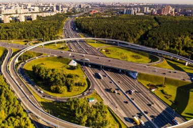 Arkaplanda insansız hava aracından çekilen şehirle karmaşık bir karşılıklı geçiş sistemine sahip bir yolun panoramik görüntüsü