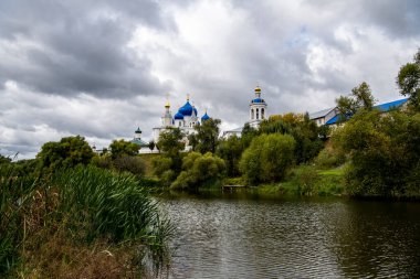 Yeşil ağaçların ve nehrin arka planında mavi kubbeler olan eski beyaz manastır.