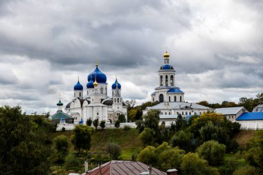 Yeşil ağaçların ve nehrin arka planında mavi kubbeler olan eski beyaz manastır.