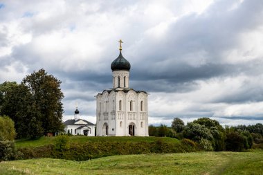 Kar beyazı, eski kilise yaz fırtınasından önce yeşil bir çayır ve gölün arka planında.